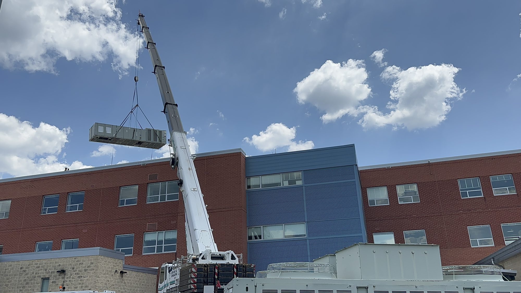 Crane lifting a new rooftop unit onto a school roof