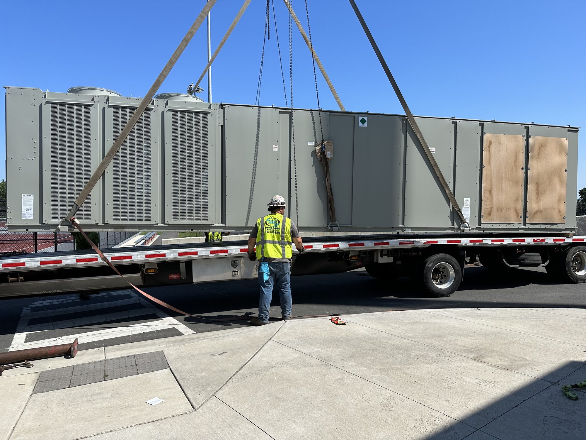 Rigging crew unloading a new Trane rooftop unit from a flatbed truck